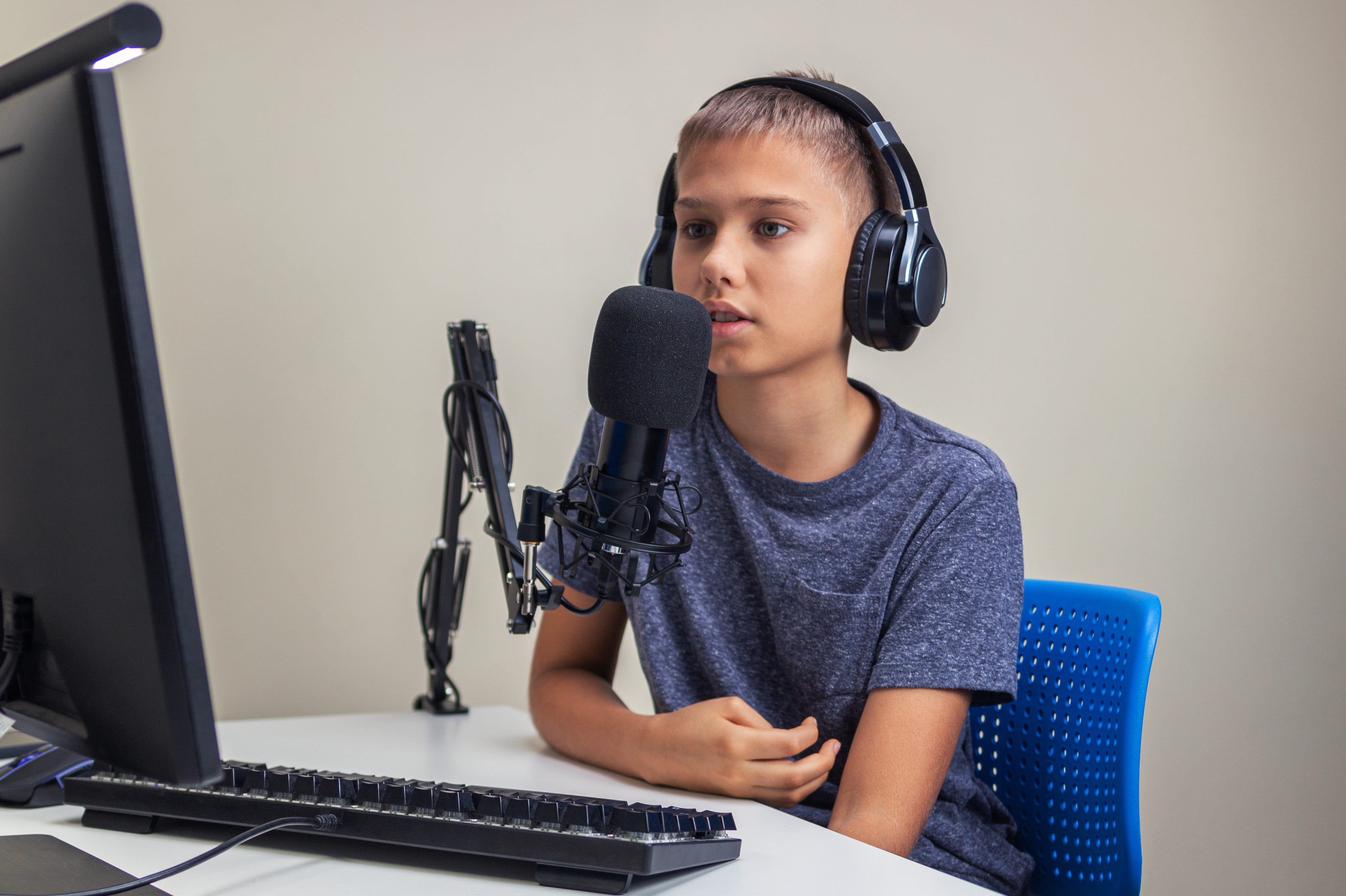 Male elementary school student wearing headphones sitting in front of microphone recording audio in Adobe Podcast.